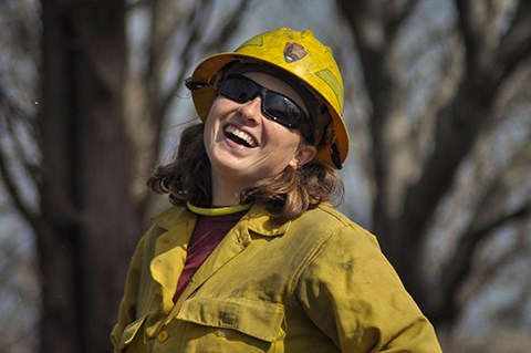 A woman wearing yellow fire resistant clothing looks at the camera while laughing.
