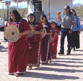 River- People-Basket-Dancers are performing. Dancers in a row followed by their singers and gourd rattle muscians.