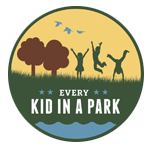 Every Kid in a Park logo of three kids playing in a field next to two brown trees.