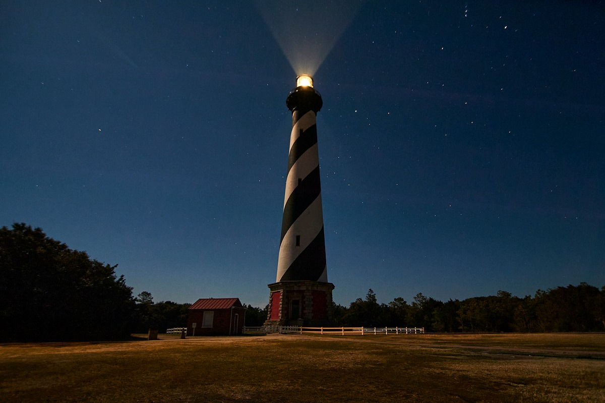 Cape Hatteras Lighthouse at Night. Light shines from lighthouse on starry night.