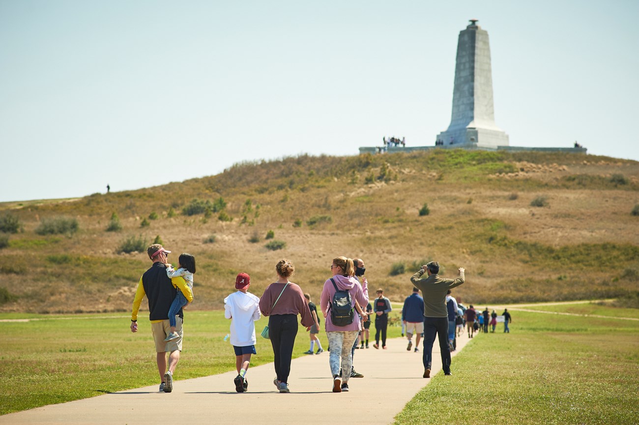 A family walks down a sidewalk toward a large monument on a hill