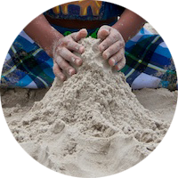 A child sculpts sand with two hands