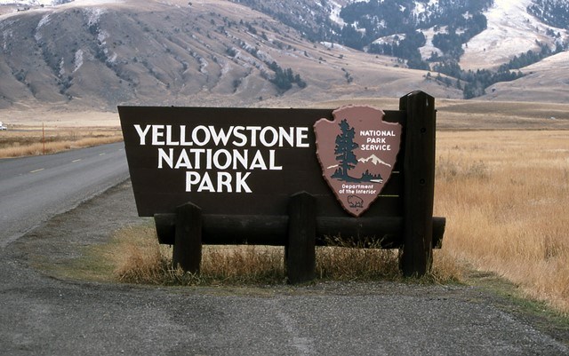 A Yellowstone National Park sign with mountains in the background.