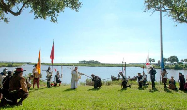 Conquistadors bearing flags watch as Pedro Menendez kisses the foot of a cross.