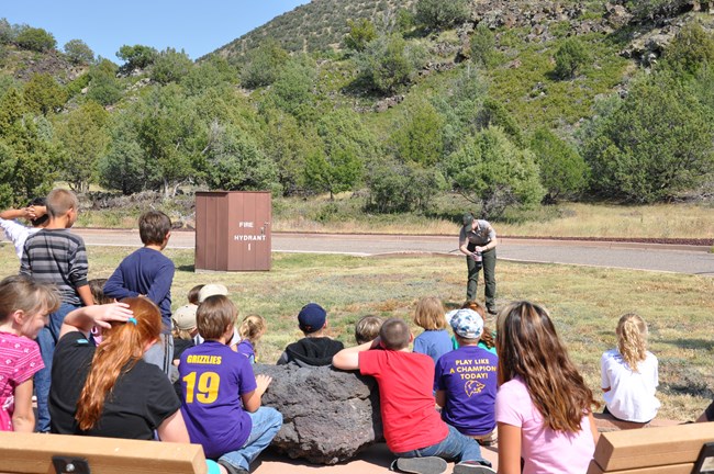 Park Ranger holds a rock while attentive young students focus on her presentation.