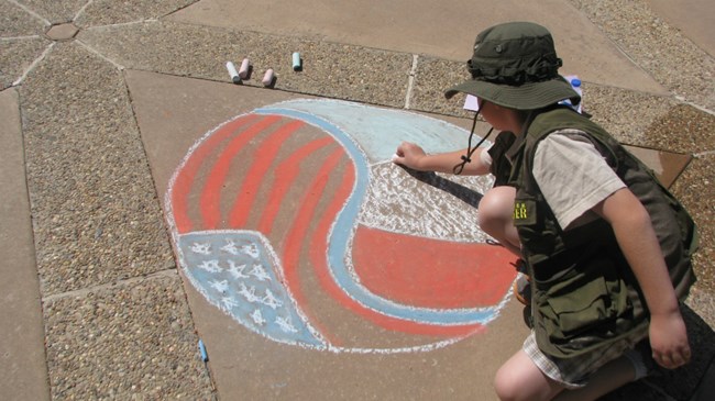 rear view of child drawing on pavement in chalk
