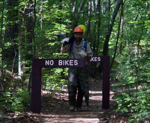 Hiker on trail through forest showing design of new bike barriers.