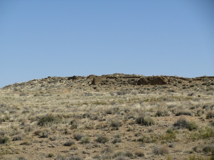 Stone walls rise out of the vast desert landscape, almost blending into the tan color of the sand immediately in the foreground.