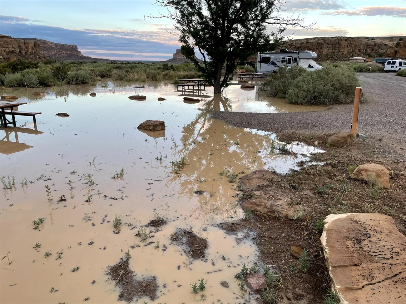 Gallo campground flood during a storm. A huge muddy collection of water floods a campground, with an RV and cars in other campsites, and a picnic table partially under the water.