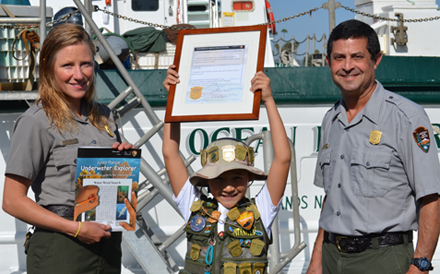 A young park visitor receiving a junior ranger award from two national park service rangers.
