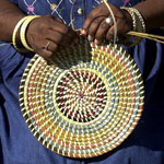 Hands of an African American woman sewing a colorful sweetgrass basket.