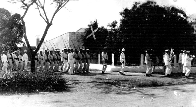 historic photo of Danish troops and military musicians marching in front of Fort Christiansvaern, ca. 1910