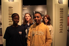 Four students stand in front of the exhibits and two columns with the words