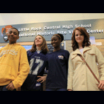 Four students pose in front of the information desk with Little Rock Central High School National Historic Site written on the wall behind them.