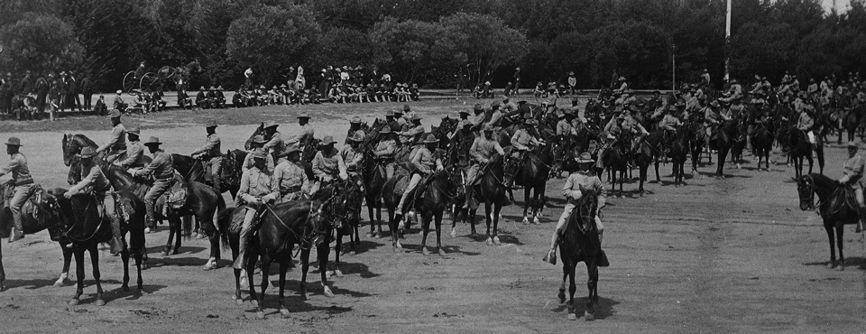 Several mounted soldiers on horses inside of a large dirt corral area.