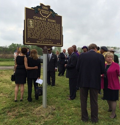Several people standing on a grassy area next to a large plaque on a post.