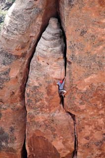 rock climber with red helmet is perched in red sandstone crack, reaching up with right hand