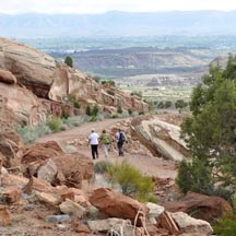 A couple walk up a gently sloping, winding path among red-orange sandstone boulders.