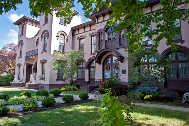 A pink stucco building with multiple windows set behind colorful gardens.