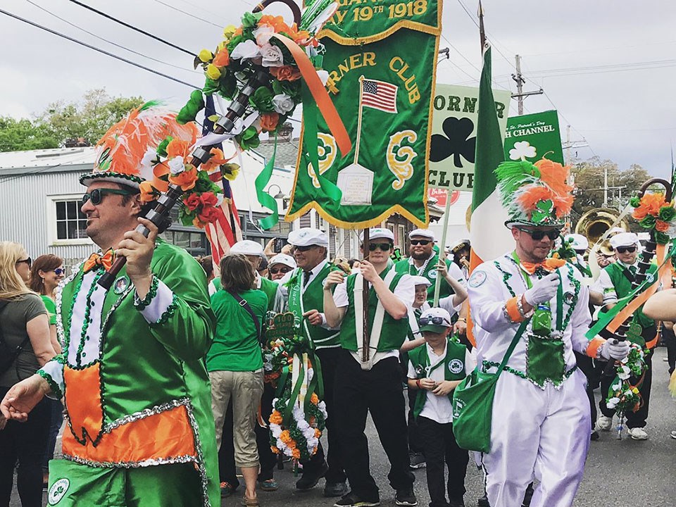 marching band and other dressed in green, orange and white silk clothes carrying banners down a street
