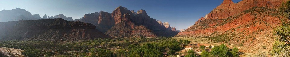 Panoramic black and white photo looking up Zion Canyon, structures are seen near the river.