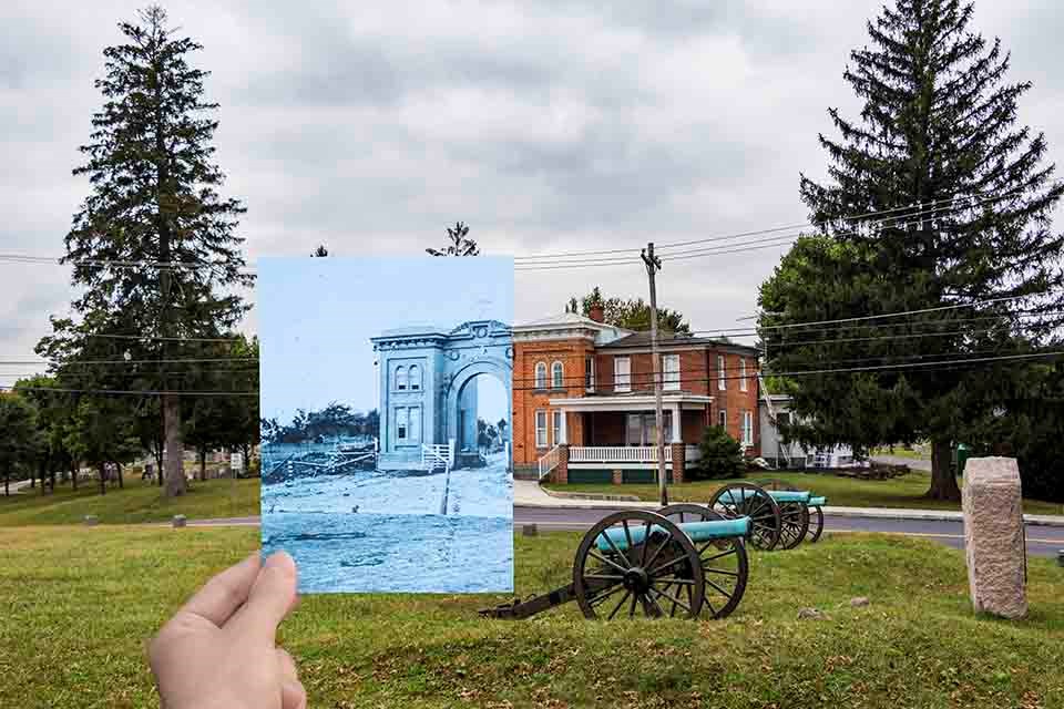 A black and white picture is superimposed on a modern picture of a red brick building shaped like an arch with two cannons in front of the structure.