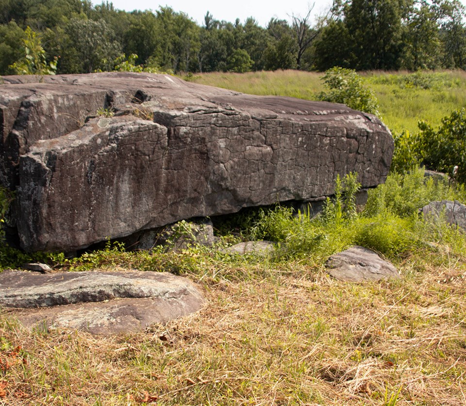 A black and white image of a dead man laying in front of a large boulder.