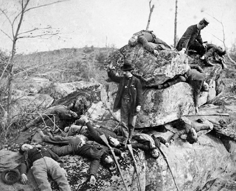 A number of men posing as dead soldiers lie across and underneath rocks in the Slaughter Pen.