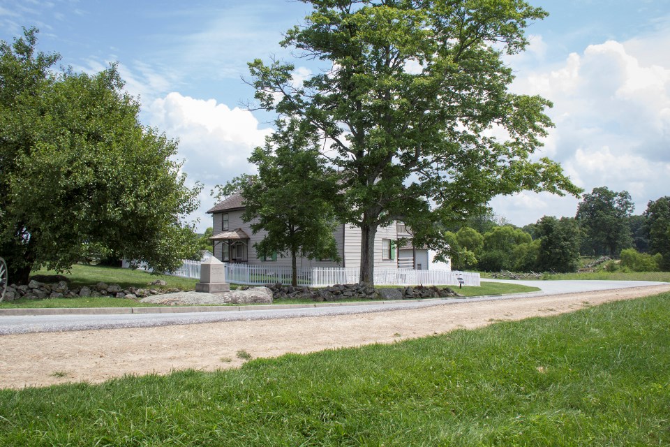 A historic picture of the Trostle house, held up in the center of the modern version, shows numerous dead horses from Bigelow's Battery.