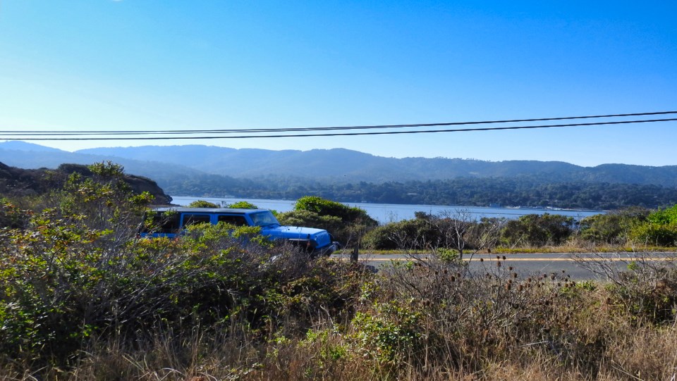 A black and white photo of a train on its side with water and hills in the background.