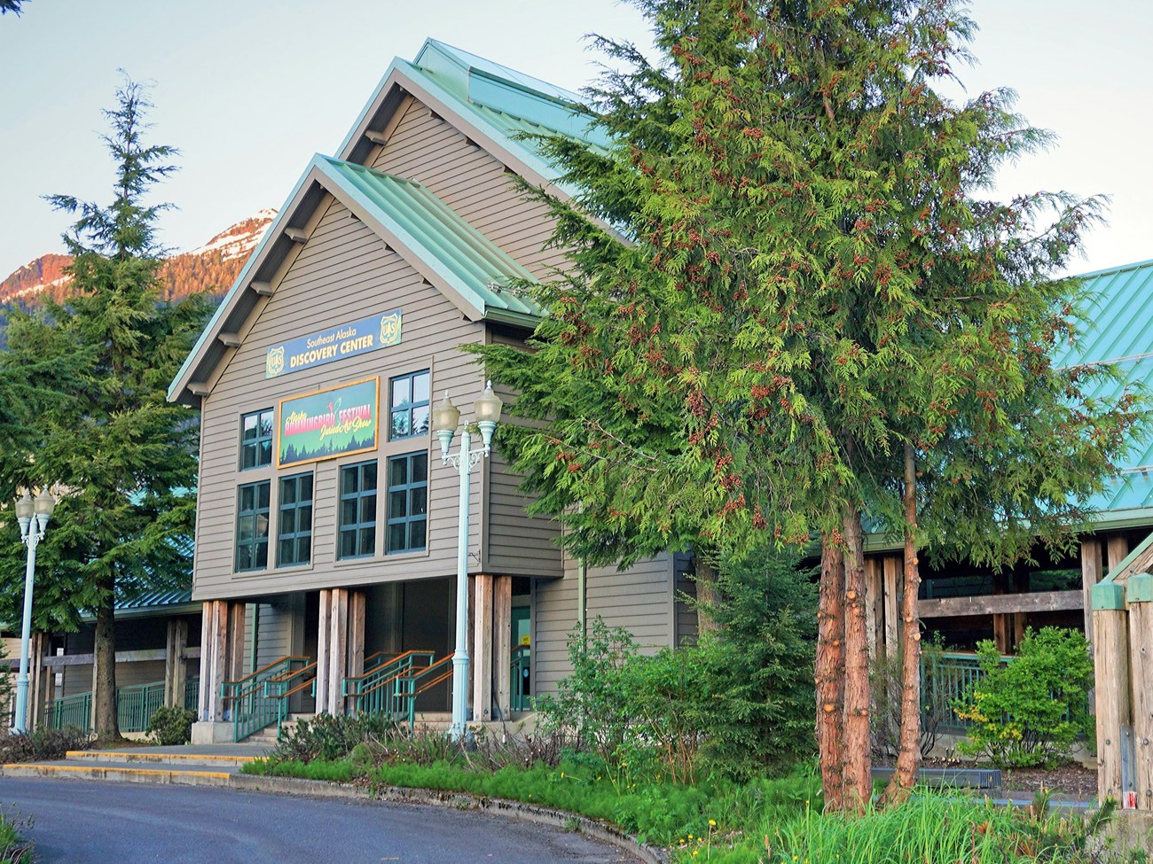 Outdoors; Large green roofed wooden building with evergreen tree next to entrance.