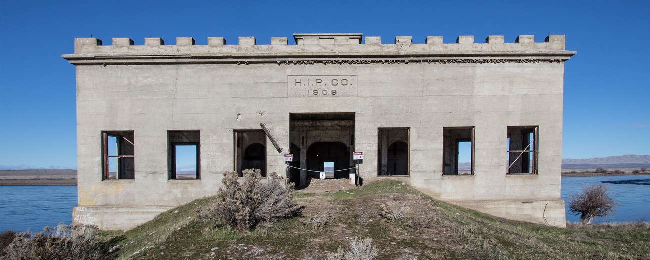 Small square cement building along a waterway. Lettering on the building reads "H.I.P.CO. 1908"