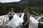park rangers putting trash into white plastic bags on a rocky beach