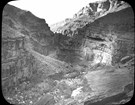 Black and white historic photo of a side canyon with a creek between towering cliffs.