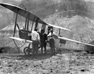 Old fashioned biplane with pilots standing nearby.