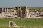 an elevated patch of prairie with steep, exposed sod stands above green grass and badlands canyons.