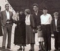 woman looks away from camera, smiling at child and surrounded by family standing in large metal pipe