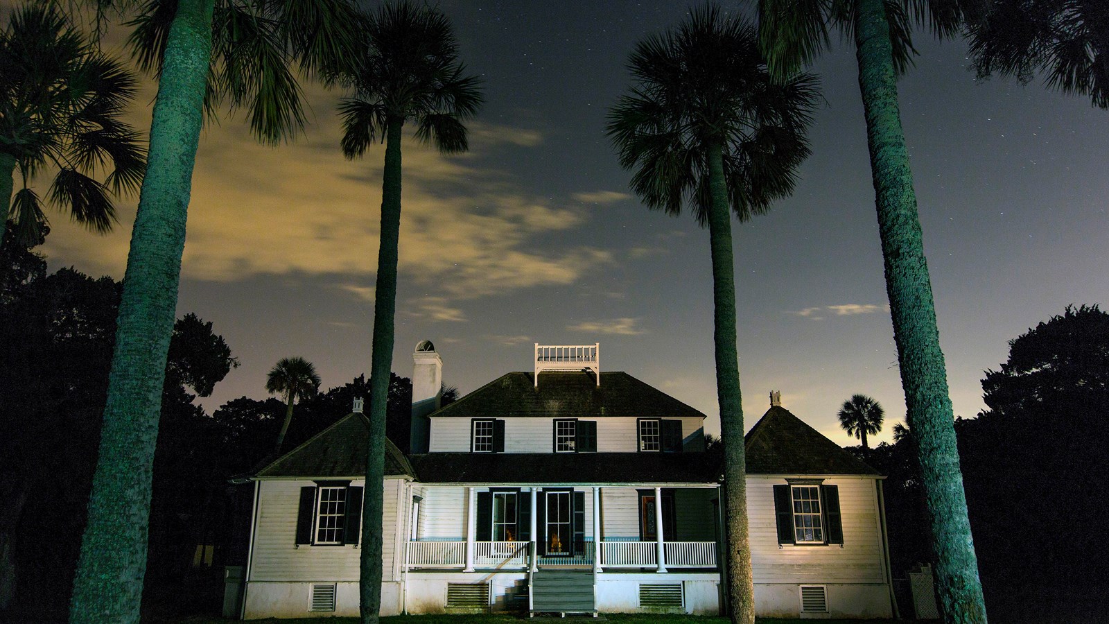 the planters home two sotry white with black shutters palm trees in from and night sky above