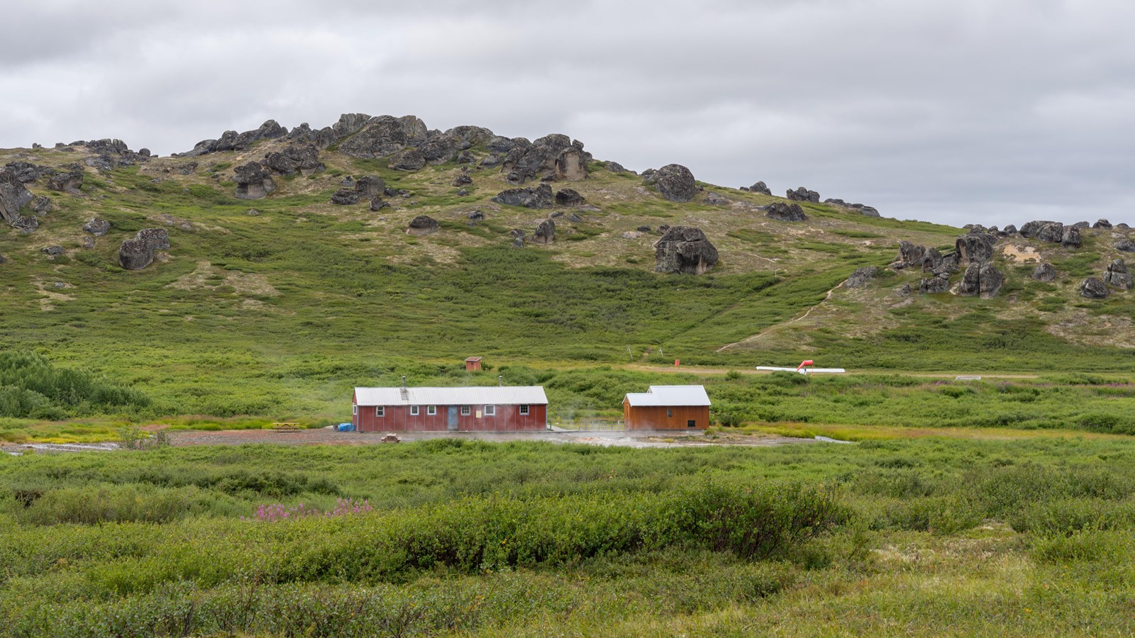 A bunkhouse and bathhouse are nestled at the base of a bowl-shaped valley.