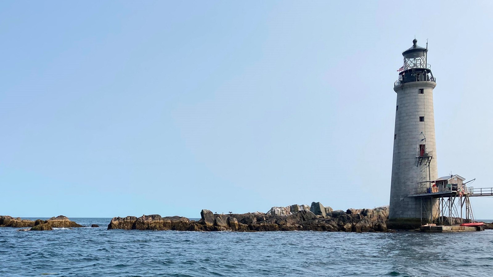 View of the rocky island looking up from the water with the grey lighthouse on the right
