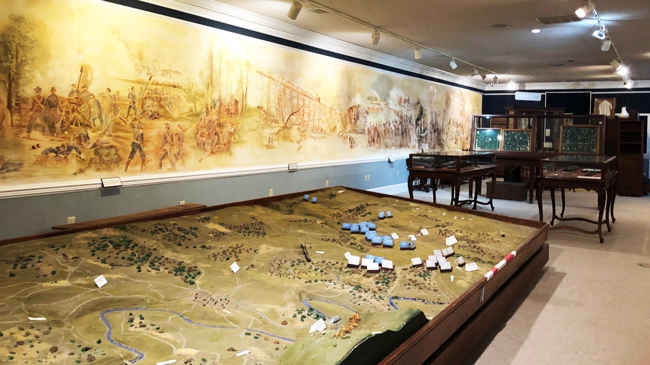 A museum exhibit hall has a battlefield diorama and mural painting.
