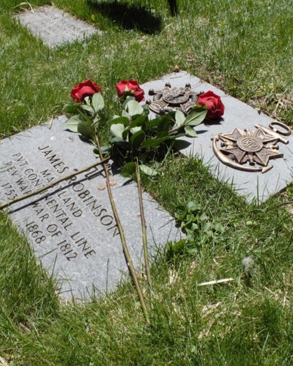 Two headstones, one with military honors, in a cemetery with red flowers resting on top.