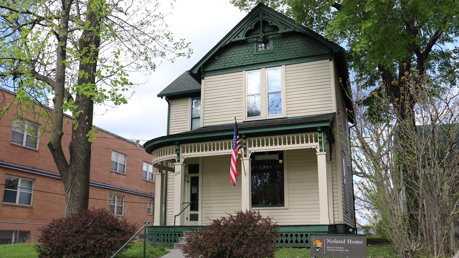 A yellow and green 2 story Victorian home with an American flag on the porch.