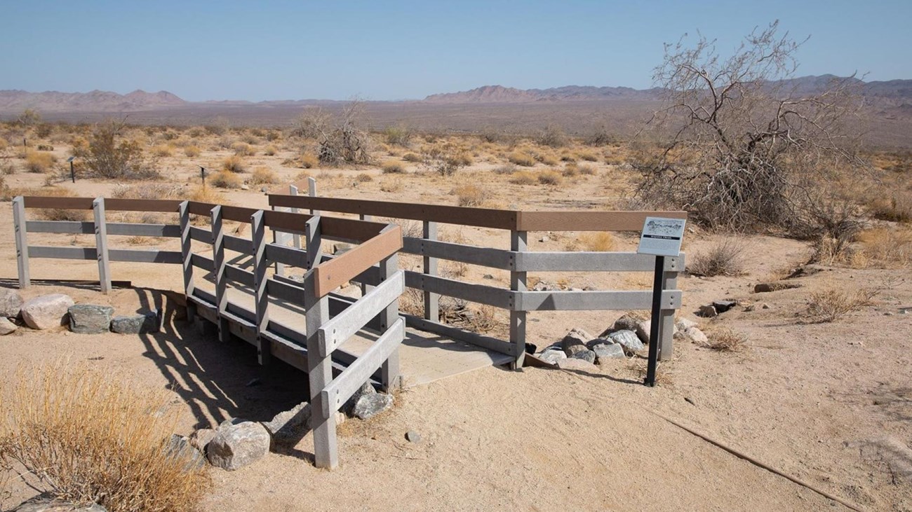 A wooden bridge over a wash with a valley filled with desert vegetation in the background. 