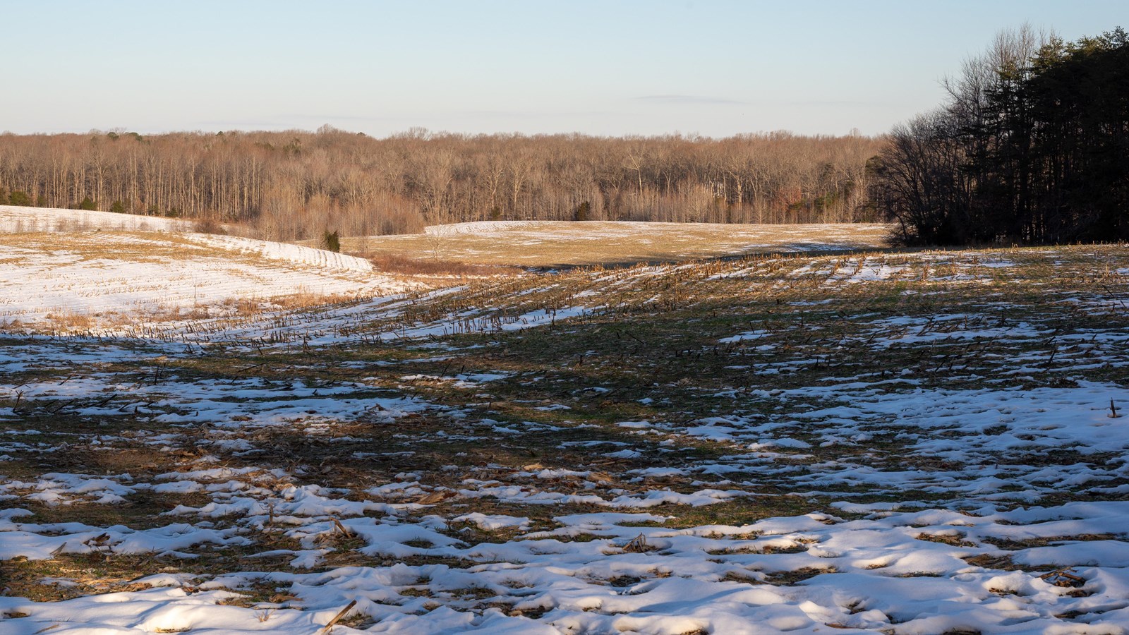 An open agricultural field with a light 1-inch layer of snow on sunny day.