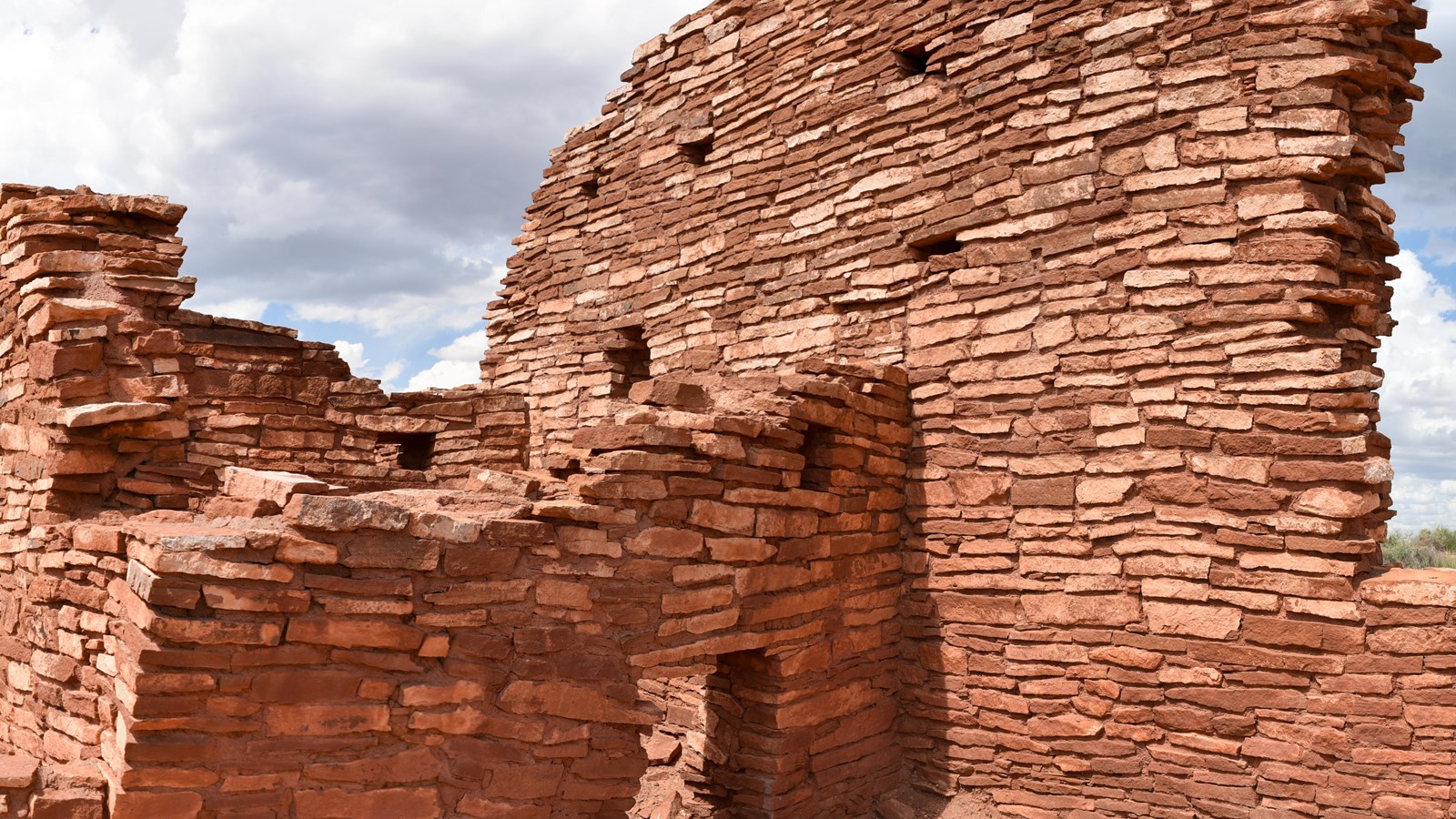 A red sandstone pueblo with a large curving wall