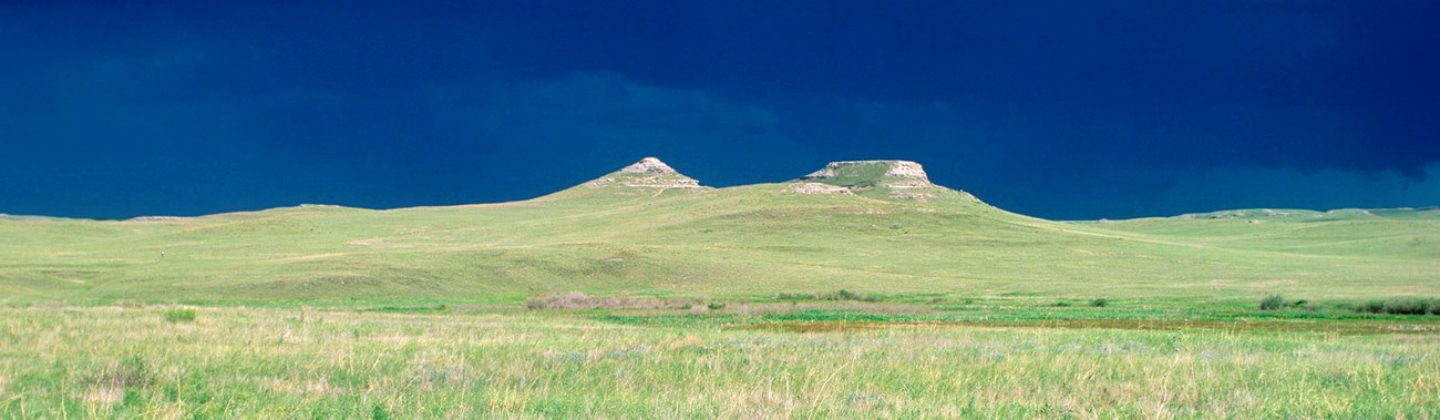 The sun illuminates the fossil hills with a dark, stormy sky in the background.