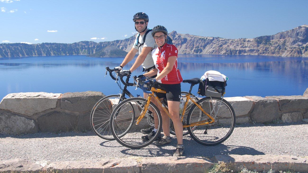 Two visitors on bikes with Crater Lake in the background.