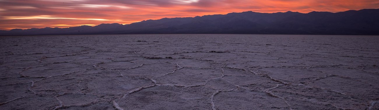An expansive salt flat with distant desert mountains and a pink sky sunset. 