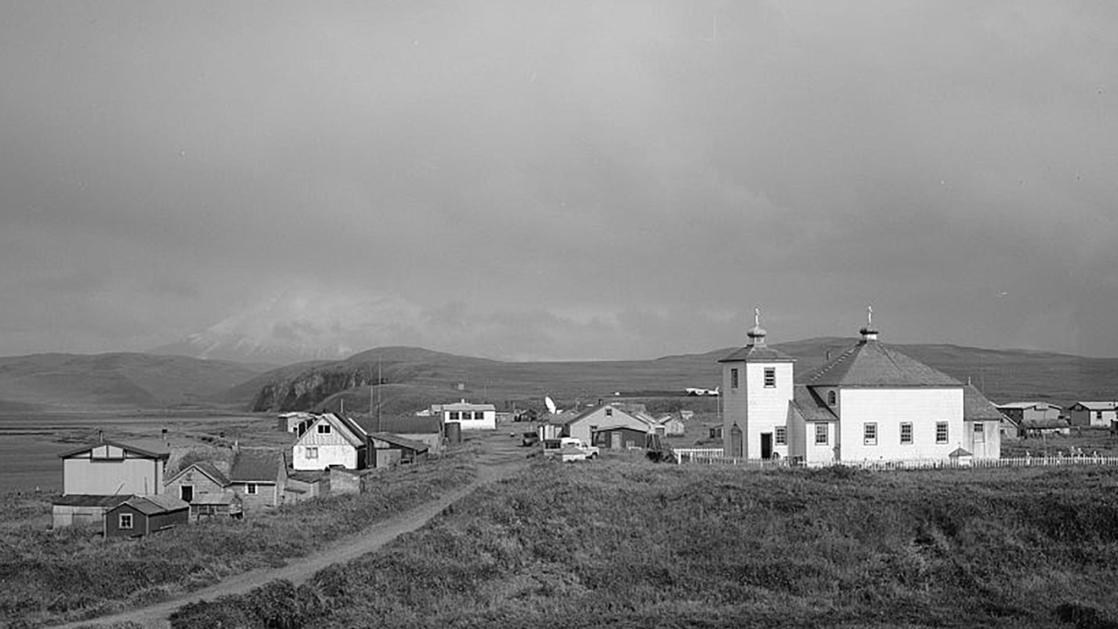 Black and white photo of Nikolski Village with a small Russian Orthodox Church in the midground.